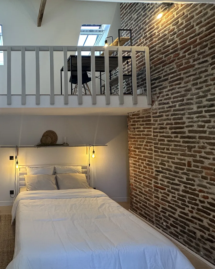 Chambre mezzanine rénovée avec mur en brique et éclairage d'ambiance